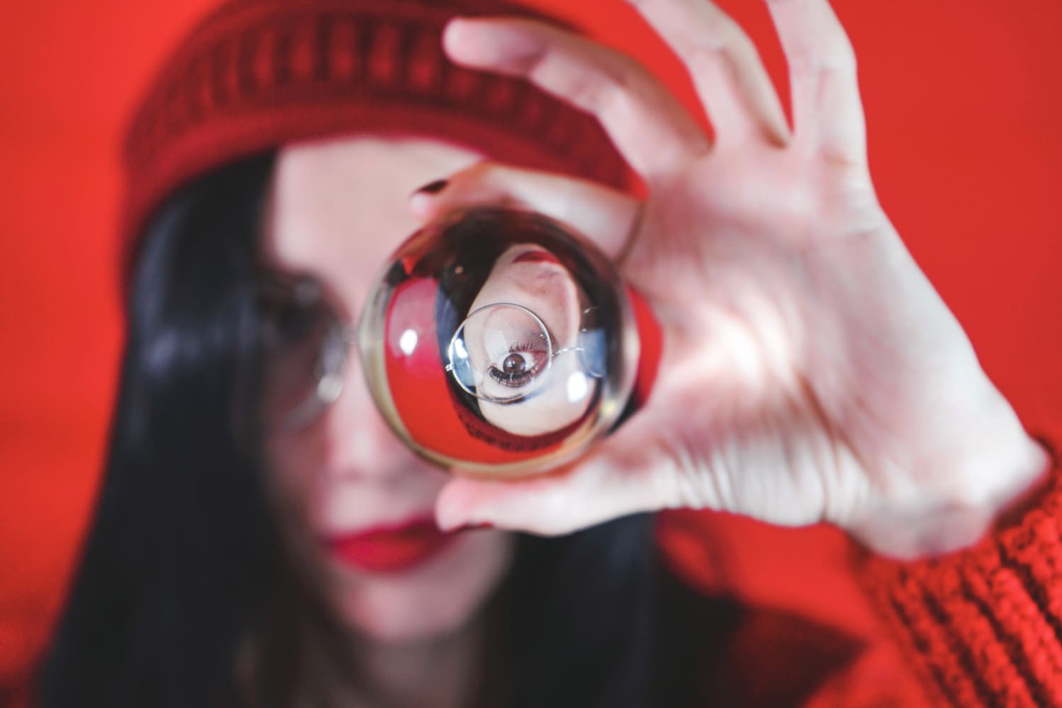 brunette woman with eye glasses holding crystal ball between thumb and pointing finger